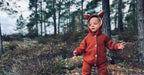 Child wearing a red fox onesie in a forest setting